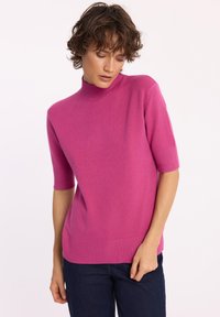 Różowy sweter z krótkim rękawem i golfem, wykonany z miękkiej tkaniny, z prążkowanymi mankietami i dołem, o luźnym kroju i gładkiej fakturze.