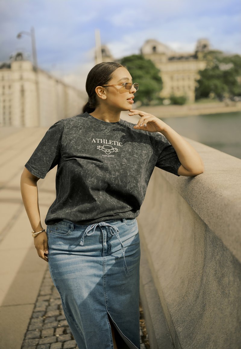 Schwarzes Marmor-Muster T-Shirt mit dem Text "ATHLETIC", kombiniert mit einem hellblauen Denim-Rock mit schlitz vorne und Kordelzugbund.