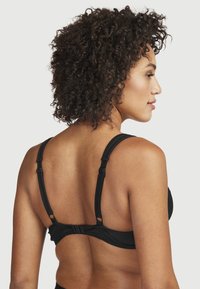 Svart bh med justerbara band, med en slät yta och en enkel design. Stängning på baksidan med hakar.