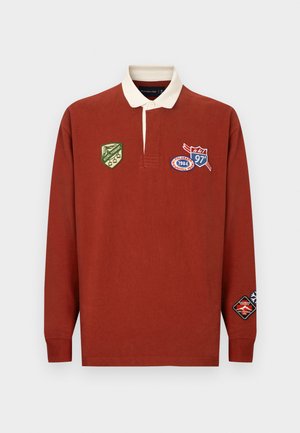 Ragbyové tričko v rezavě oranžové barvě s dlouhými rukávy, krémovým límcem a několika nášivkami s různými barvami a vzory na přední straně.
