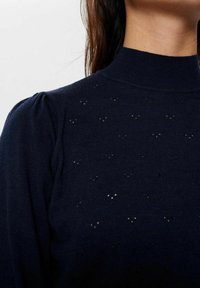 Marineblauwe gebreide pullover met een hoge kraag, met subtiele open steekenpatronen en pofmouwen, wat zorgt voor een gestructureerde uitstraling.