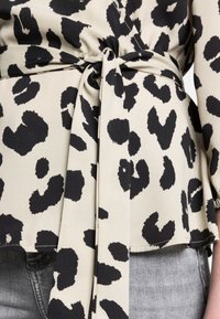 Top avvolgente con stampa leopardo in crema e nero, caratterizzato da un dettaglio con vita legata, con una texture di tessuto morbida, abbinato a jeans grigi sbiaditi.