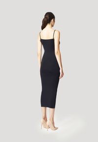 Zwarte aangesloten midi-jurk met dunne bandjes, met een gladde textuur en slanke silhouette. Gemaakt met nude hoge hakken.