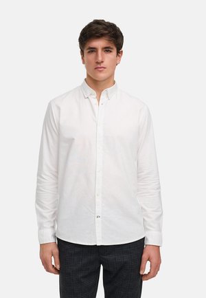 Chemise blanche à manches longues avec un col, texture lisse et coupe décontractée. Présente une patte de boutonnage et des boutons sur le devant.