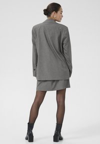 Grijze krijtstreep blazer met een iets oversized pasvorm, gecombineerd met een bijpassende rok. Model draagt zwarte hoge laarzen en doorschijnende panty’s.