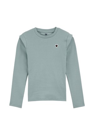 T-shirt à manches longues et à côtes en vert pâle avec un col rond, présentant un petit emblème de cœur noir et blanc sur la poitrine.