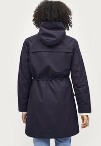 Marineblauwe lichte regenjas met een trekkoord in de taille, lange mouwen en een capuchon. Glad materiaal met een rechte snit en minimale details.