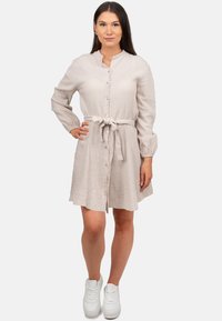 Abito button-up beige chiaro con maniche lunghe, tessuto testurizzato, cintura legata in vita e vestibilità comoda, abbinato a sneakers bianche.