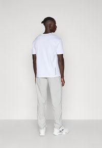 Witte T-shirt met korte mouwen en een losse pasvorm, gecombineerd met lichtgrijze broek en witte sneakers met zwarte accenten. Eenvoudig, modern ontwerp.