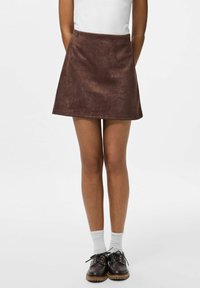 Brun ruskinds mini nederdel med en svajet silhuet, parret med hvide sokker og mørke snørebåndssko. Enkel, glat tekstur.