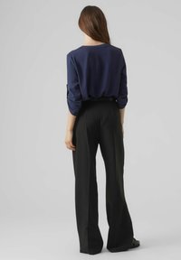 Donkerblauwe lange mouw top gecombineerd met hoge taille, wijde zwarte broek. Glad materiaal en een relaxte pasvorm. Eenvoudig ontwerp zonder patronen.