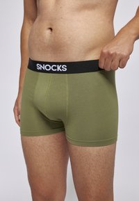 Olivgrüne Herren-Boxershorts mit einem schwarzen elastischen Bund, der mit weißem "SNOCKS"-Branding versehen ist, weichem Material und eng anliegendem Design.