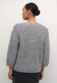 Pulover gri tricotat cu o croială liberă și scurtă, mâneci largi și un model texturat. Gulerul și manșetele ribbate completează designul general.
