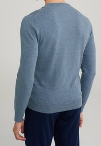 Light blue crewneck sweater in soft fabric, featuring long sleeves and ribbed hem. Back view shows smooth texture and fitted design.