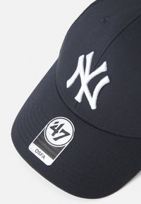 Marineblå baseballcaps med hvit brodert "NY"-logo, laget av stoff med en jevn tekstur, med et merke som har logo og "OSFA."