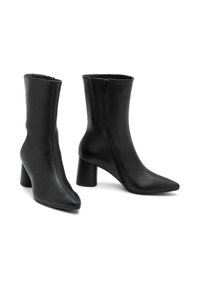 Par de botas de cuero negras de media caña con cremalleras laterales, puntas afiladas y tacones gruesos, mostradas sobre un fondo blanco.