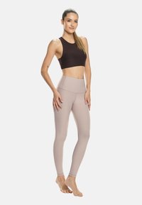 Rjav športni modrček in svetlo bež visokorasle legice iz raztegljive tkanine, ki se ponašajo z gladko teksturo in oprijetim dizajnom.