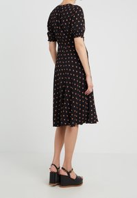 Vestido negro con mangas cortas abullonadas y patrón floral naranja. Diseño de falda acampanada y tela suave. Llevado con sandalias de cuña negras.