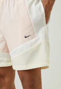 Nike sportinės šortai, pasižymintys šviesiai rožine viršutine dalimi, balta vidurine dalimi ir šviesiai geltona apatine juostele su juodu logotipu.