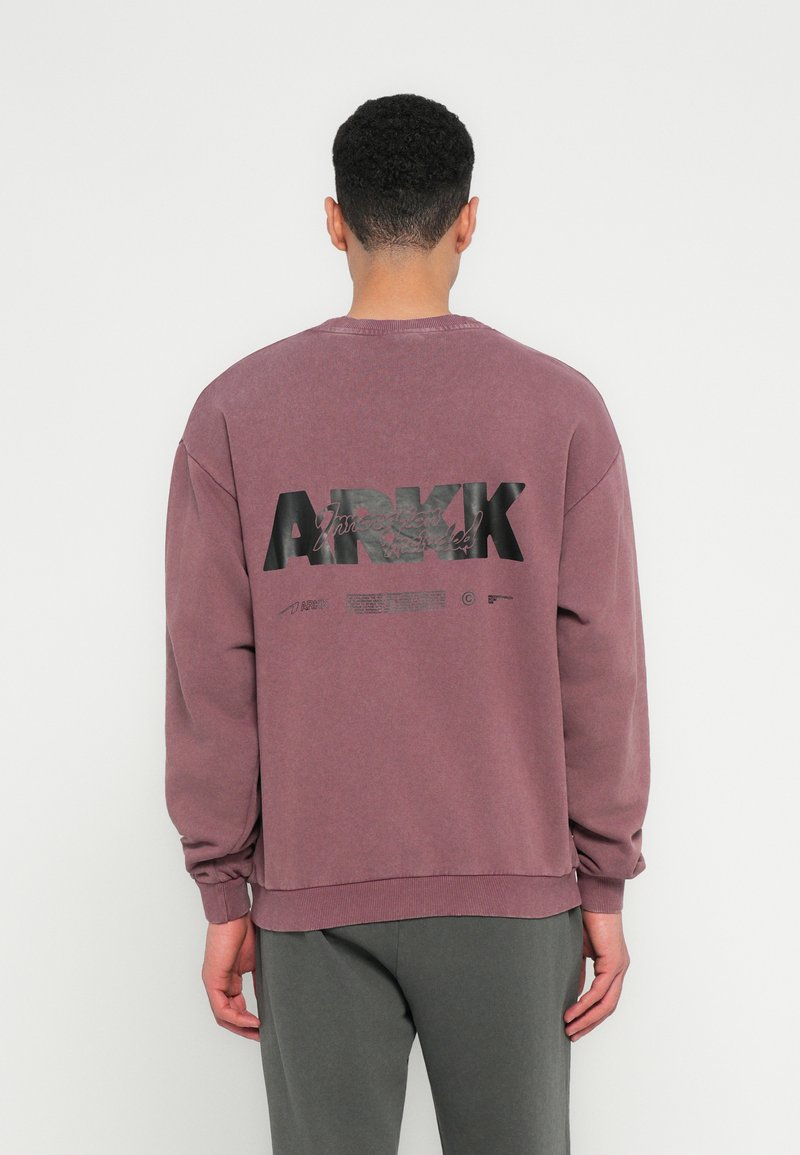 Bordeauxfarbener Sweatshirt mit Rundhalsausschnitt und gerippten Bündchen, featuring ein großes schwarzes "ARKK"-Logo und Text auf der Rückseite. Aus Baumwollmischgewebe.
