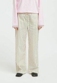 Wide-leg, cream-colored pants with thin brown stripes, featuring a drawstring waist and smooth texture, paired with black slip-on shoes.