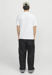 Hvid bomulds t-shirt parret med mørke denim bukser, der har optrullede manchetter og gule sting på baglommen, båret med en grøn kasket.