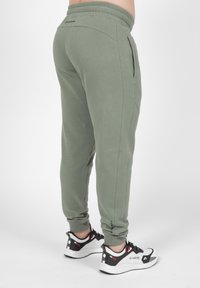 Khaki joggers met een elastische tailleband, zijzakken en taps toelopende manchetten, gecombineerd met zwart-witte sport sneakers.