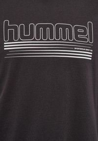 Czarna bawełniana koszulka z wyrazistym białym logo "hummel", z poziomymi paskami i tekstem „SPORTSWEAR SINCE 1923” poniżej.