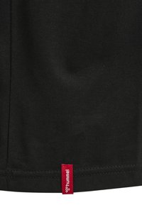 Zwarte stof met zichtbare stiksels aan de onderzoom en een klein rood label met de tekst "hummel" bevestigd aan de naad.