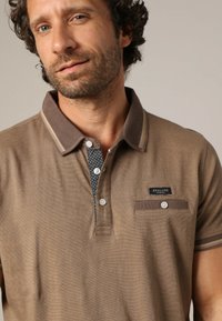 Polo shirt marron en tissu texturé, avec un col contrastant et une patte de boutonnage, des détails imprimés à l'intérieur et une poche poitrine avec un patch logo.