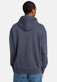 Sudadera de algodón azul marino con una amplia capucha ajustable, hombros caídos y puños acanalados; tiene una textura suave y un corte relajado.