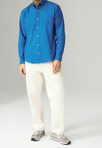Camisa azul de botones con mangas largas, pantalones color crema y zapatillas grises con detalles blancos y suelas negras. Estilo simple y casual.