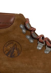 Bottines de randonnée en daim marron présentant des œillets métalliques, des lacets rouge-brun et un logo de montagne sur le côté. Bordure en cuir lisse sur le haut.