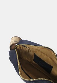 Borsa in pelle blu navy con una cerniera dorata, dotata di un interno beige, una tasca interna e una tracolla decorata.