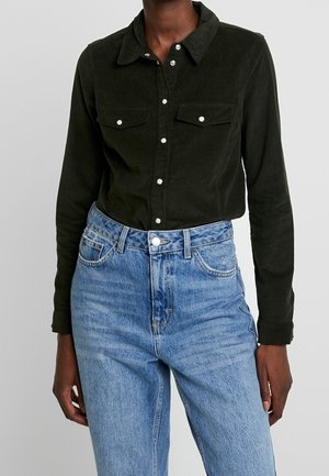 Mørkegrøn kordduk button-up skjorte med to brystlommer og sølvknapper, parret med højtaljede lyseblå denim jeans.