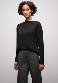 Zwarte, gestructureerde trui met lange mouwen en een ronde hals; gecombineerd met grijze geruite broek met knoopdetails aan de zijkanten.