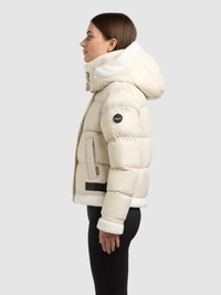 Kurtka puchowa w kolorze kremowym, miękki kołnierz i mankiety z futerka syntetycznego, pikowana tekstura, gumowa naszywka z logo na rękawie, czarny akcent u dołu.