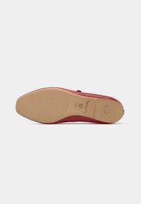 Semelle de chaussure rouge avec une base en caoutchouc beige lisse, présentant un motif texturé et des détails de logo. Conçue pour le confort avec un léger soutien de la voûte plantaire.