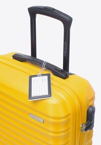 Žlutý tvrdý kufr s vodorovnými drážkami, černou teleskopickou rukojetí, visačkou na zavazadla a logo deskou. Zapínání na zip a boční zámek.