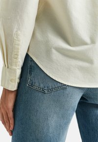 Cream striped button-up shirt with long sleeves, paired with blue denim jeans featuring a back pocket and tapered leg design.