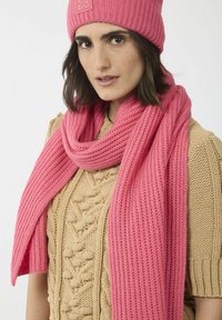 Un bonnet en tricot côtelé rose et une longue écharpe assortis à un pull beige texturé, comprenant un motif en tricot à torsades et un col rond.