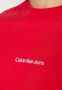 Red cotton t-shirt with a smooth texture and a crew neck. Features a white embroidered logo "Calvin Klein Jeans" on the front.