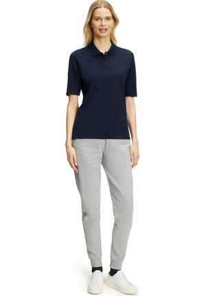 Marineblauwe polo met een kraag en drie knopen, gecombineerd met lichtgrijze joggingbroeken en witte sneakers met elastische manchetten.