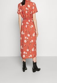 Abito midi floreale rosso con maniche corte e vita imbottita. Il tessuto è leggero; indossato con stivali neri alla caviglia. Design semplice e femminile.
