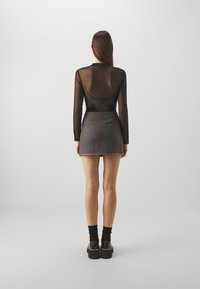 Bodysuit negro transparente de mangas largas con escote en la espalda, combinado con una falda corta gris con tachuelas metálicas en el dobladillo. Calzado negro con suelas gruesas.