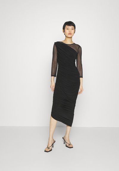Czarna midi sukienka z teksturowanej tkaniny, dopasowany krój, długie przezroczyste rękawy i asymetryczne marszczenia, zestawiona z sandałami na cienkim obcasie.