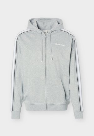 Sweat à capuche zippé gris clair avec des rayures blanches et noires sur les manches, des poches avant, une capuche avec cordon et le logo Calvin Klein sur la poitrine.