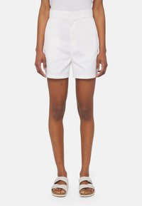 Pantaloni corti bianchi in cotone con vita alta, parte anteriore piatta e tasche. Texture morbida e vestibilità su misura, abbinati a sandali di colore chiaro.