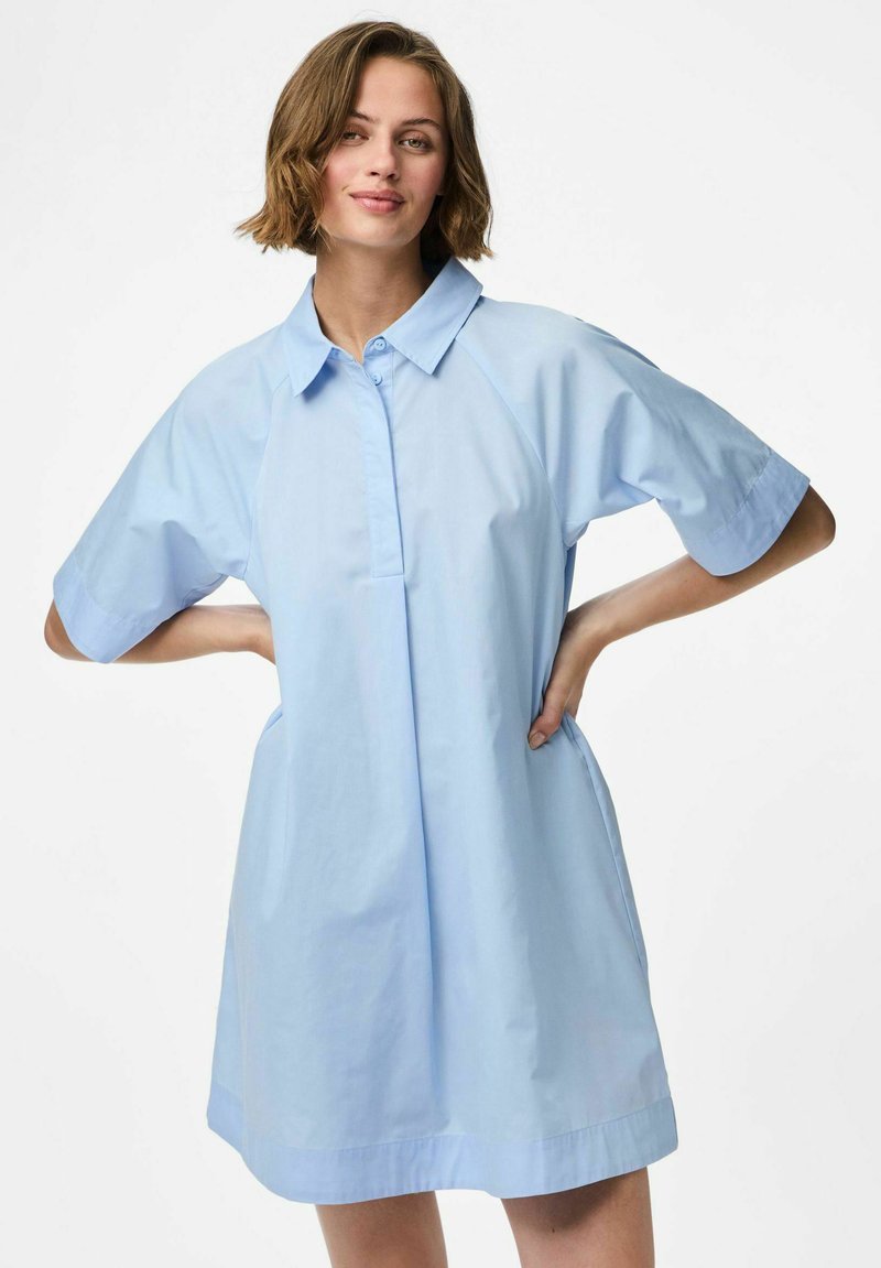 Robe chemise bleu clair avec un col, manches raglan courtes, poches latérales et une coupe décontractée, fabriquée dans un tissu doux.