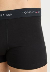Fekete pamut boxer alsónadrág kék gumírozott derékkal, amelyen a "TOMMY HILFIGER" logó fehér színben látható. Lapított varrásokkal és testhezálló dizájnnal rendelkezik.